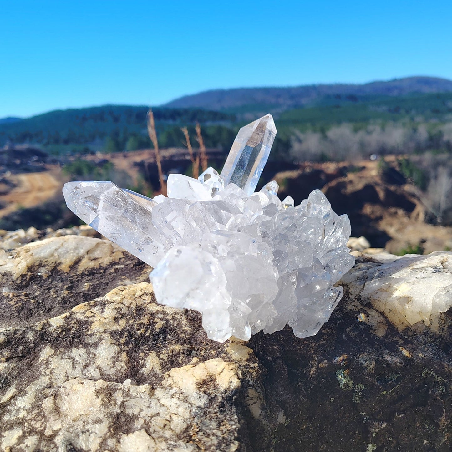 This is the right side of this quartz crystal cluster on a rock with a mountainous landscape in the background.