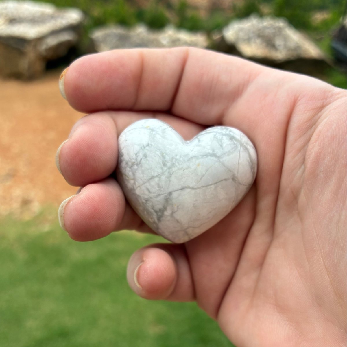 Polished white heart in a palm of a hand, and outdoors.