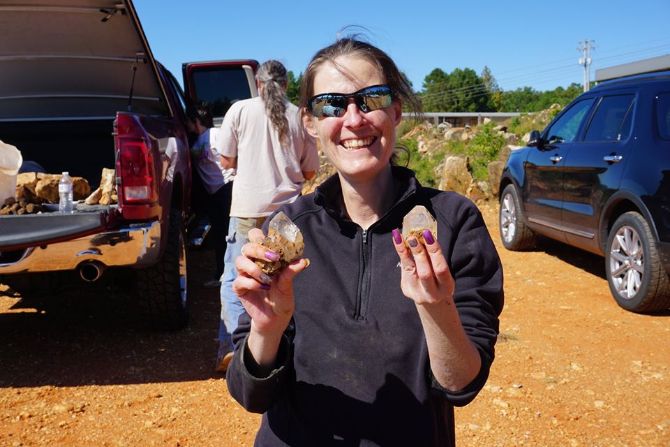 Woman holding crystals in front of several cars and a man in the background