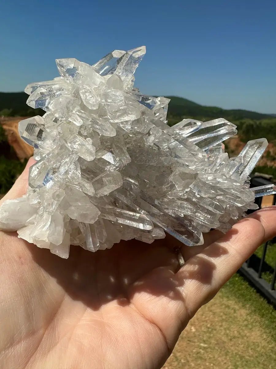 Quality Small Water Clear Crystals held in a hand with sky in the background