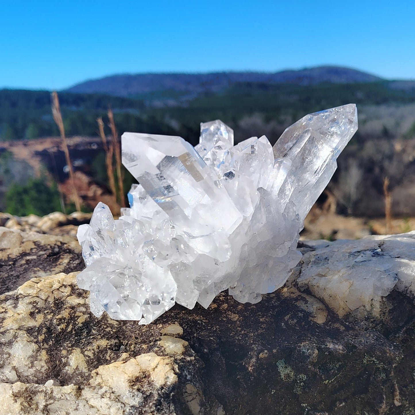 This is the left side of this Quartz crystal cluster on a rock with a mountainous landscape in the background.