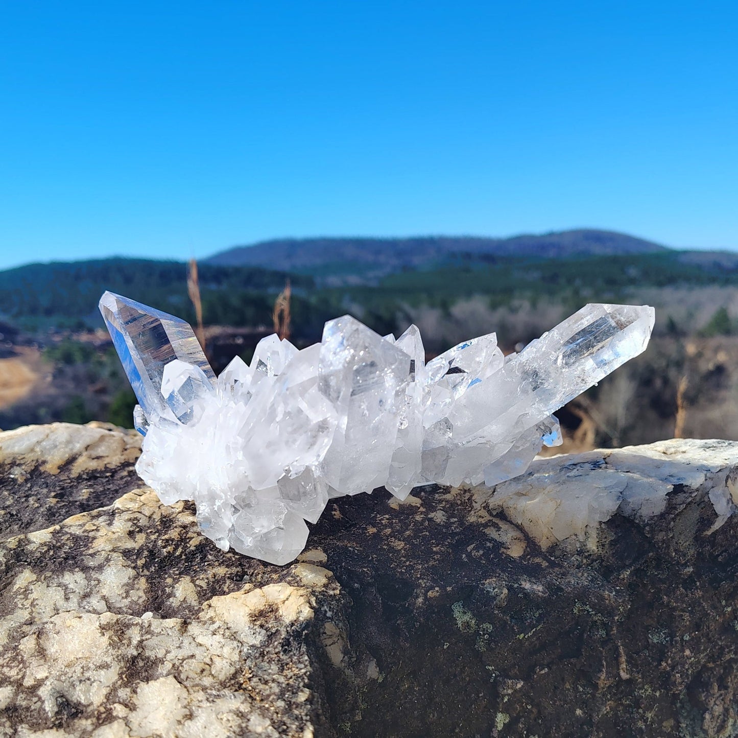 This is the back side of this Quartz crystal cluster, on a rock with a mountainous background.