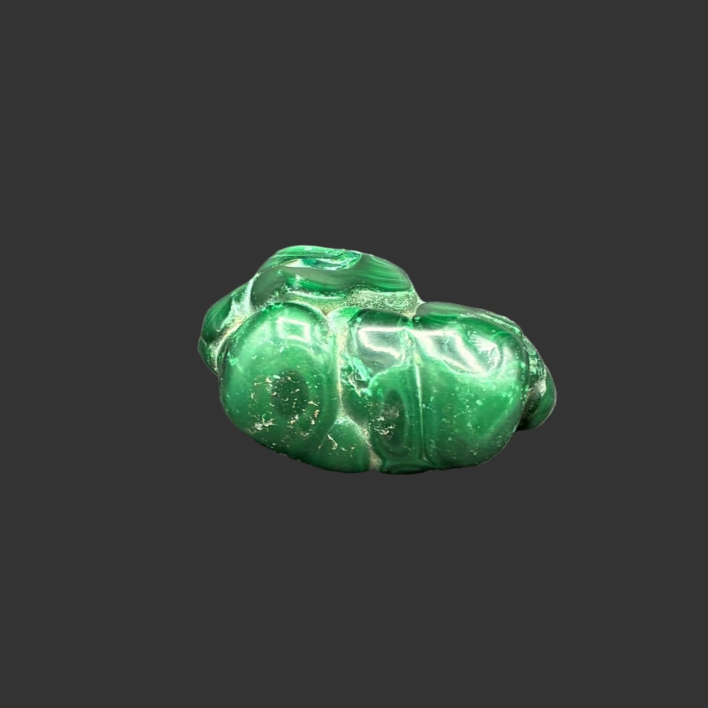 Back side of this polished green Malachite specimen in front of a black background.