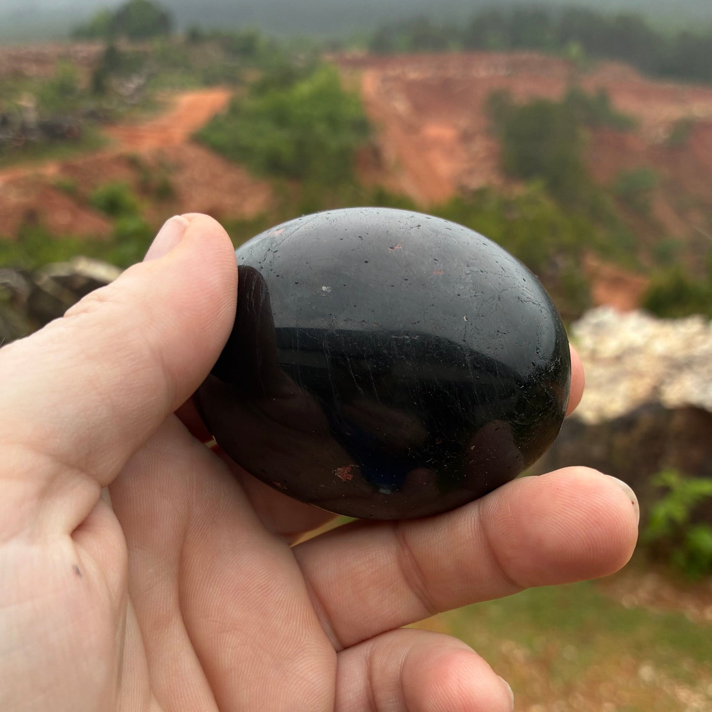 Polished oval-shaped black Tourmaline palm stone, in outdoor natural light.