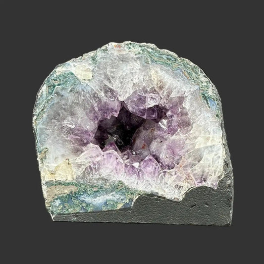 Front view of this purple Amethyst geode cathedral, in front of a black background in indoor lighting.