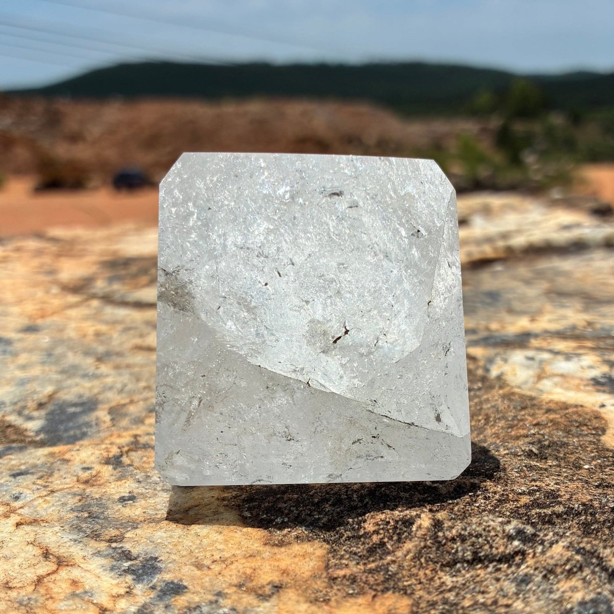 Right side of this polished and cut clear Brazilian quartz piece, sitting on a boulder outdoors.