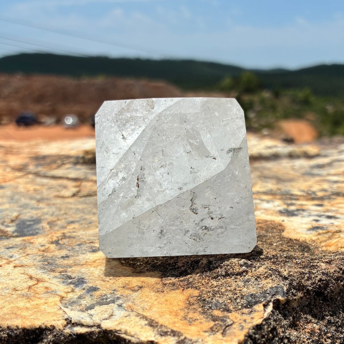 Front side of this polished and cut clear Brazilian quartz piece on a boulder outdoors.