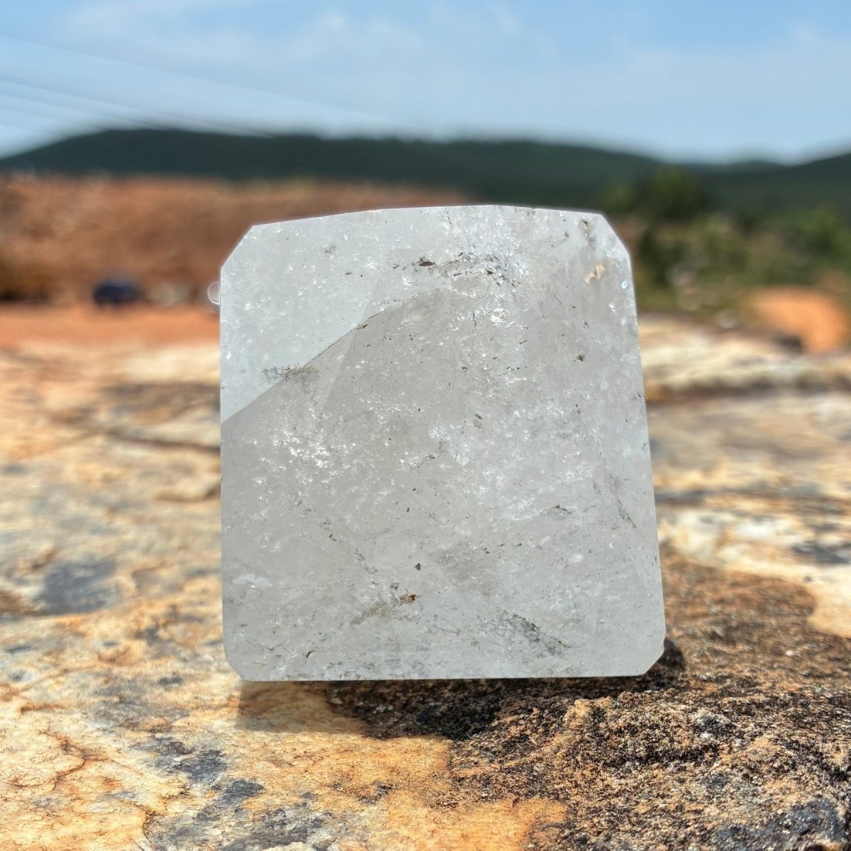Left side of this polished and cut clear Brazilian quartz piece, on a boulder and outdoors.