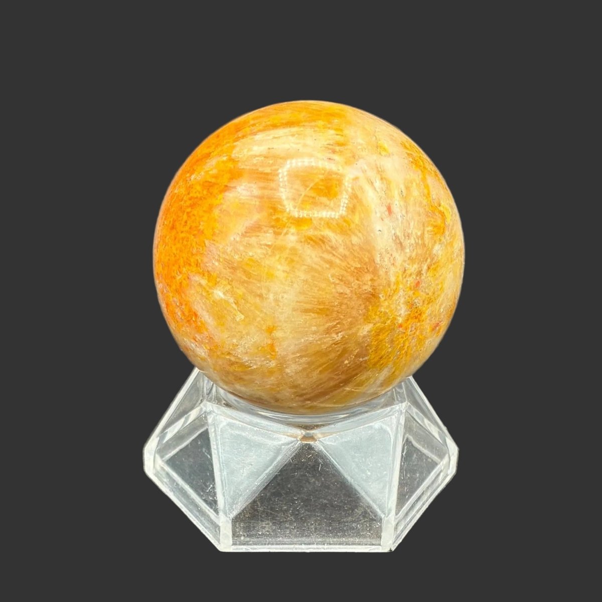 Back side of this polished Bumblebee Jasper sphere on a clear acrylic stand, in front of a black background.