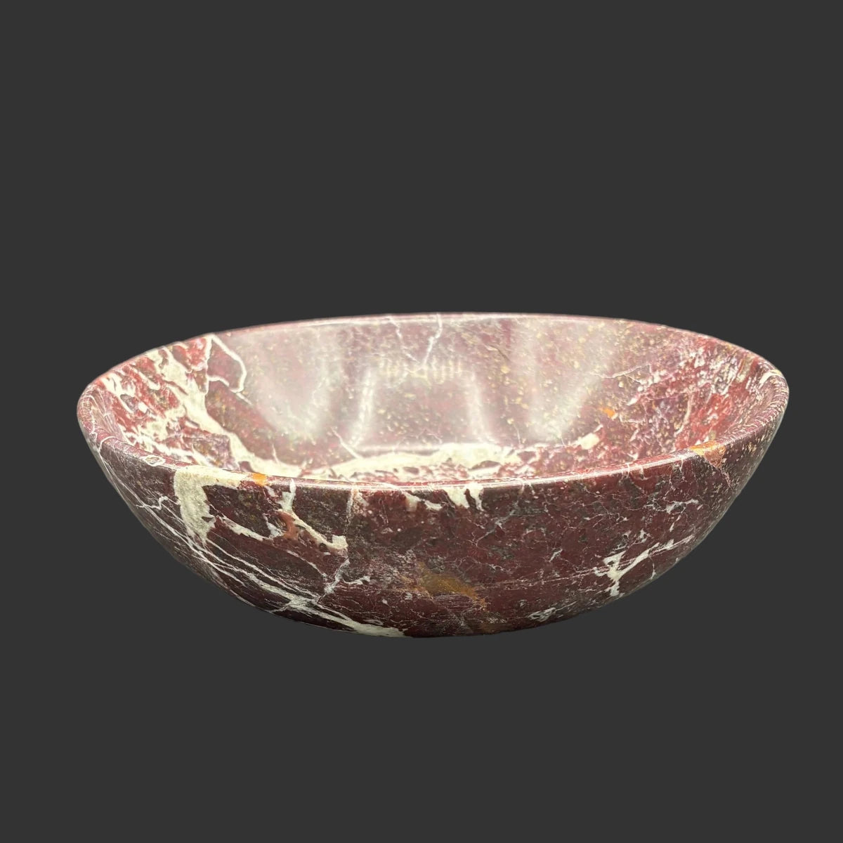 Side view of this red onyx bowl, in front of a black background.