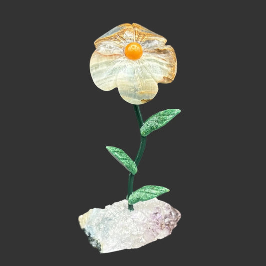 Carved blue onyx flower on a amethyst crystal base, in front of a black background.