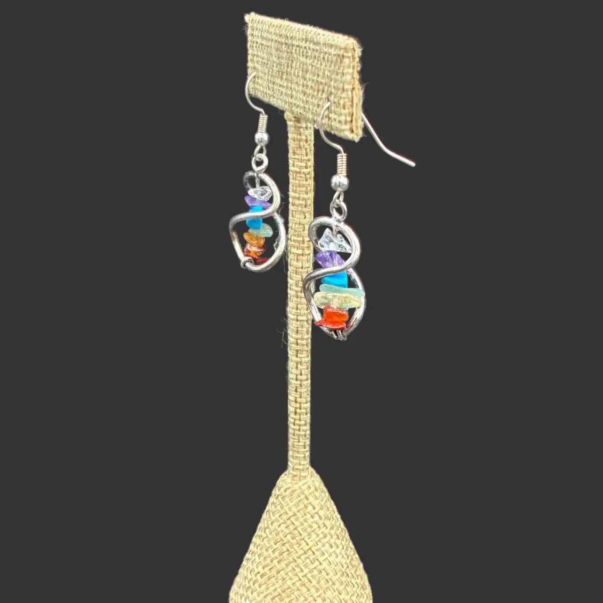 Side view of these chakra crystal chip infinity earrings in front of a black background.