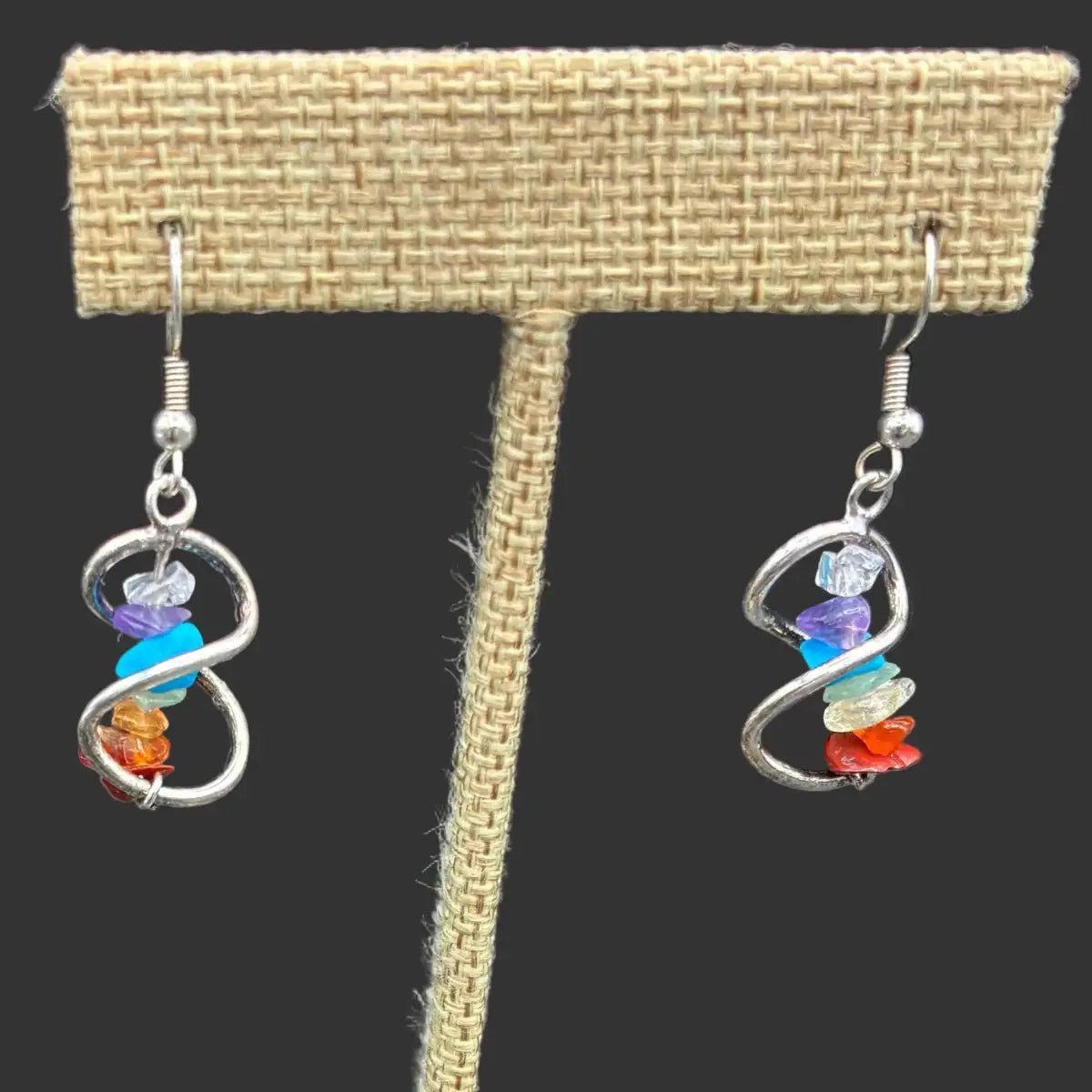 Close up of chakra crystal chip infinity earrings, in front of a black background.