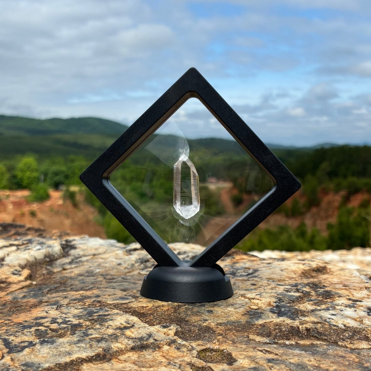 Other side of this water clear quartz crystal point, in a clear frame with base, and outdoors on a boulder.