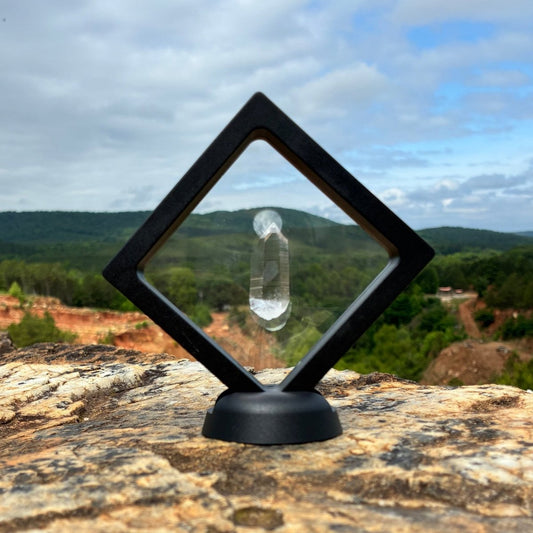 Water clear quartz crystal point, in a clear frame with base, and on a boulder outdoors.