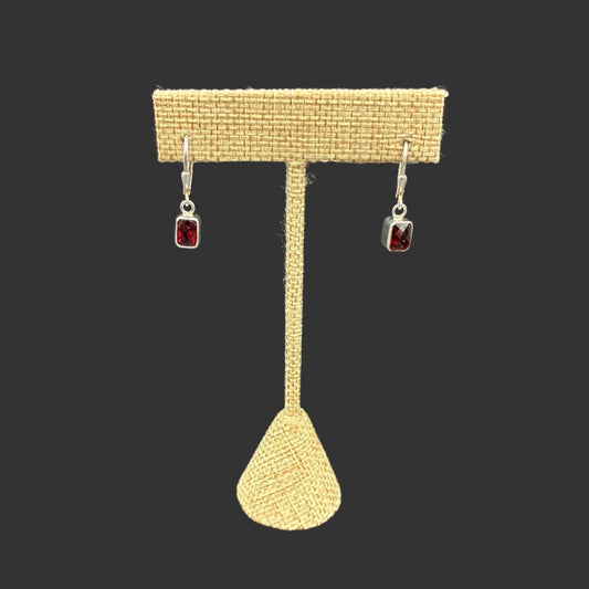 Front view of these garnet dangle earrings, in front of a black background.