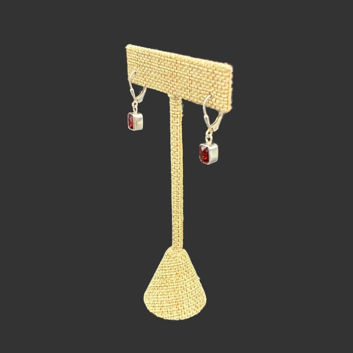 Side view of these garnet dangle earrings in front of a black background.