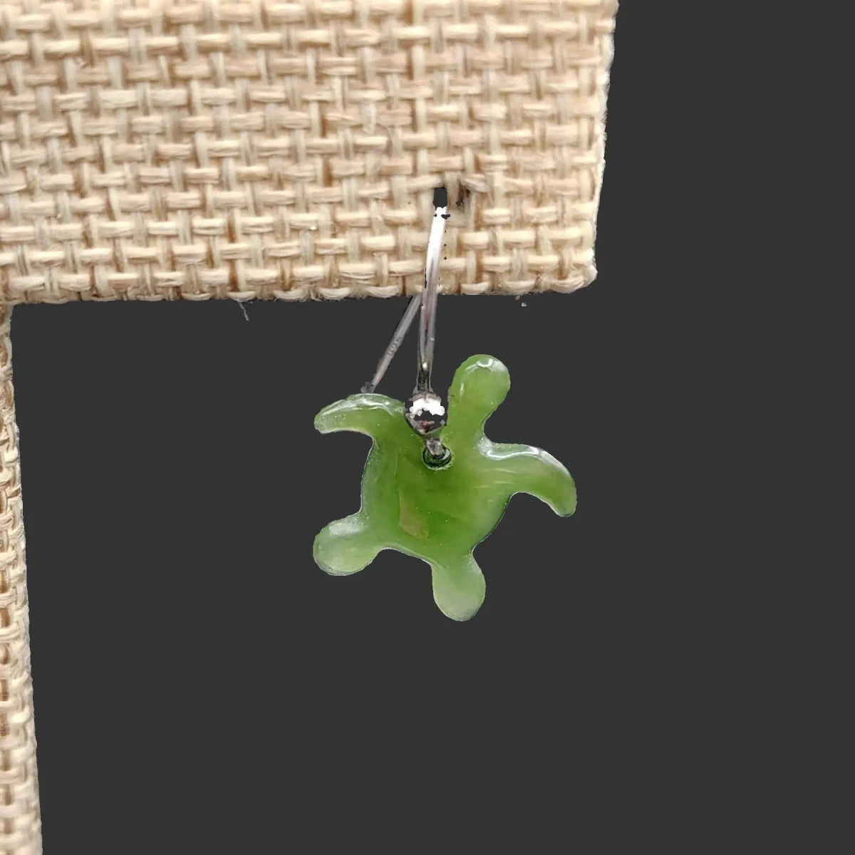 This is a close up of one of the polished green jade sea turtle earrings on a burlap display stand .