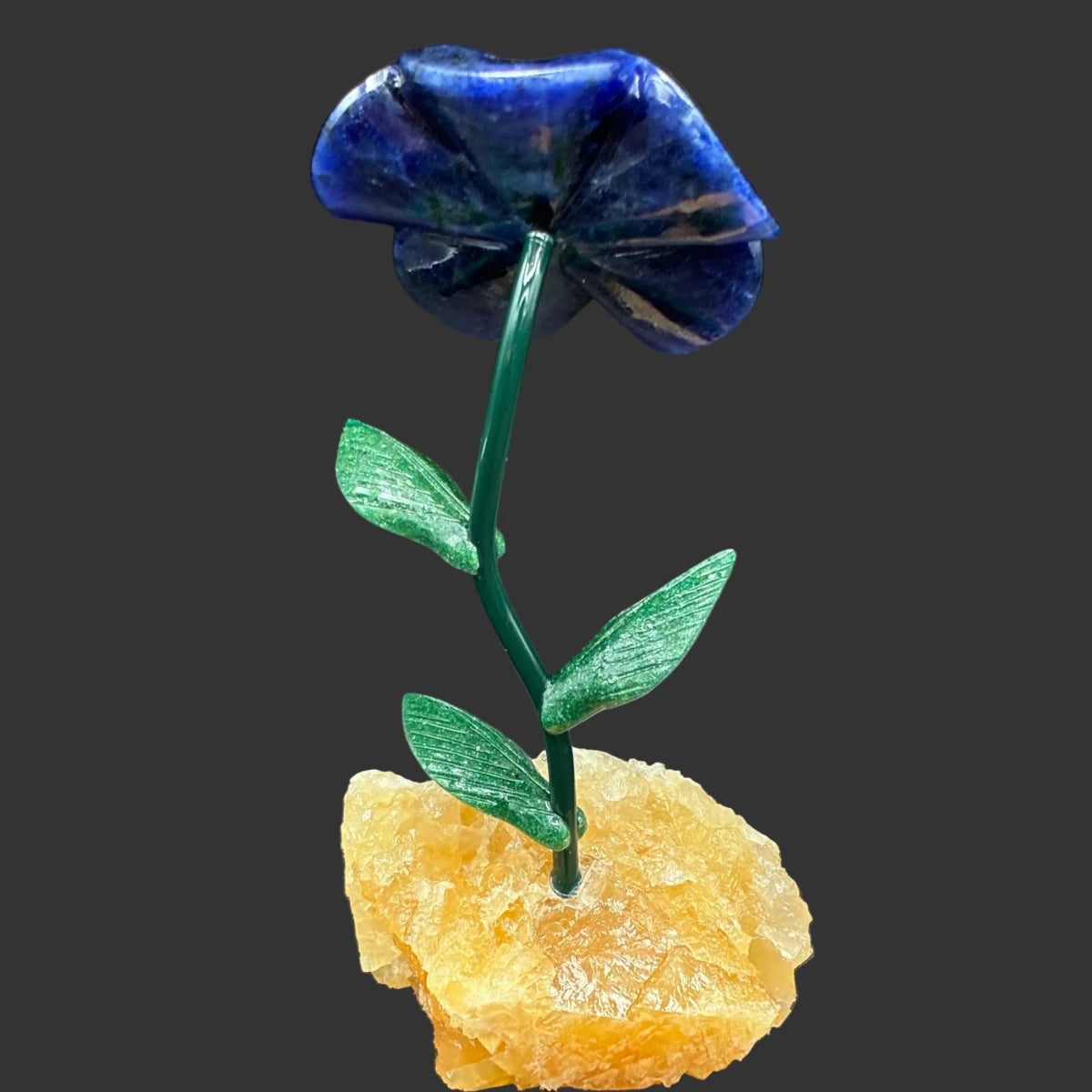 Back side of this polished blue Sodalite daisy flower, on a yellow calcite base, and in front of a black background.