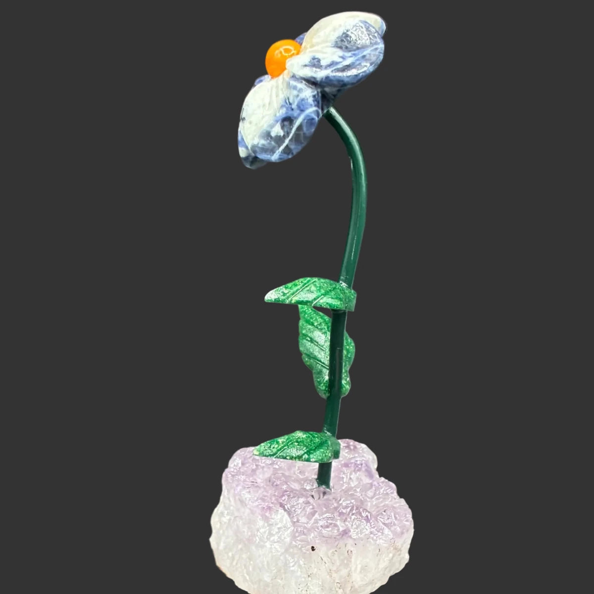 Side view of this sodalite daisy flower on a amethyst crystal base, in front of a black background.