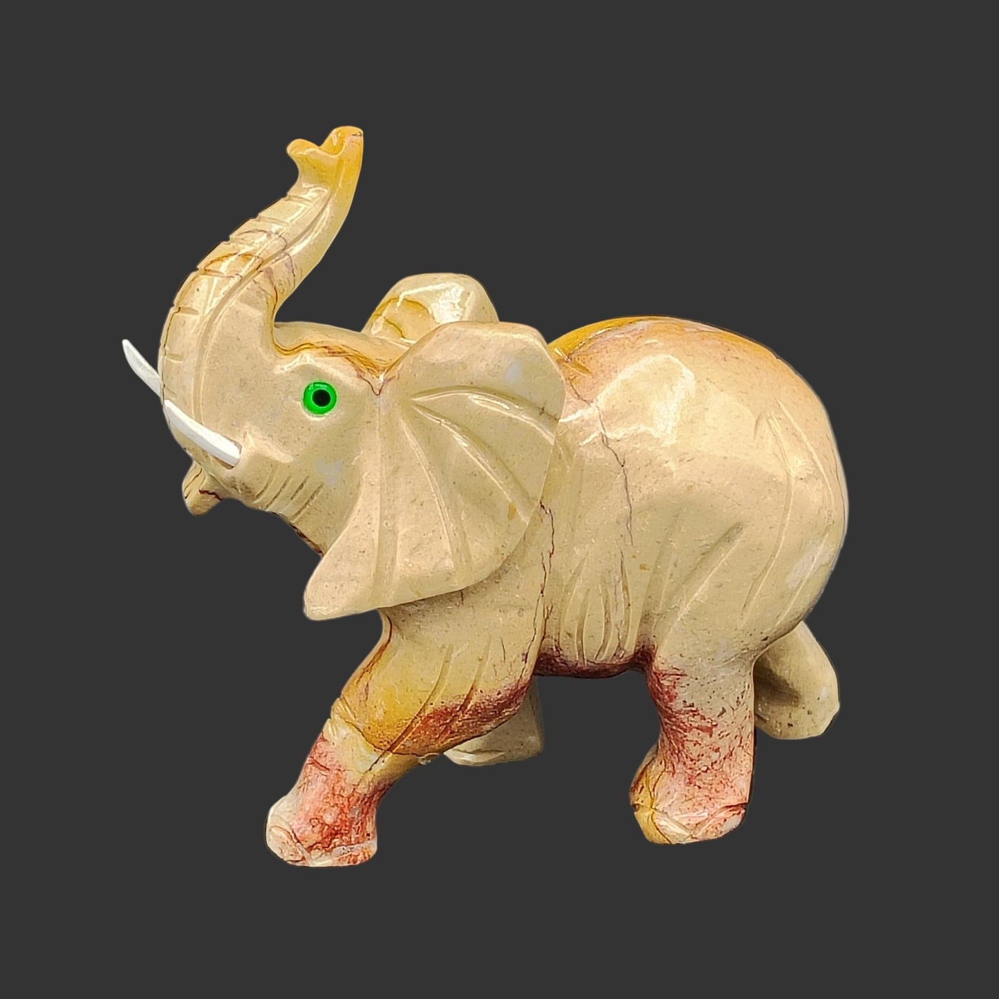 This is the left side of this hand-carved soapstone elephant. It is beige and red in color, with white tusks.