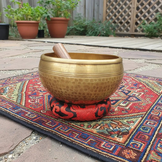 This singing bowl has hammered by hand, in Tibet, and is in a outdoor patio setting on a rug.