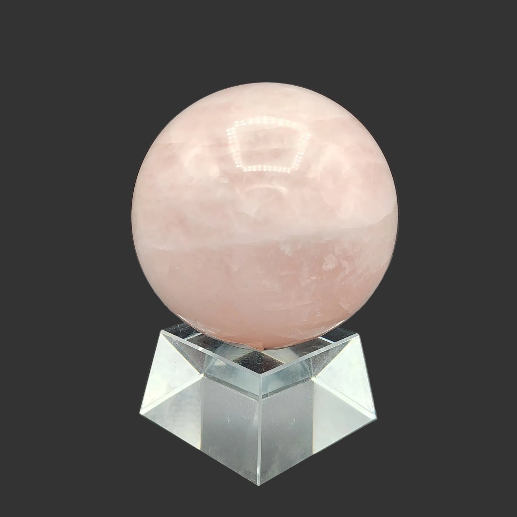 This is the back side of this polished pink rose Quartz sphere on a clear square stand.