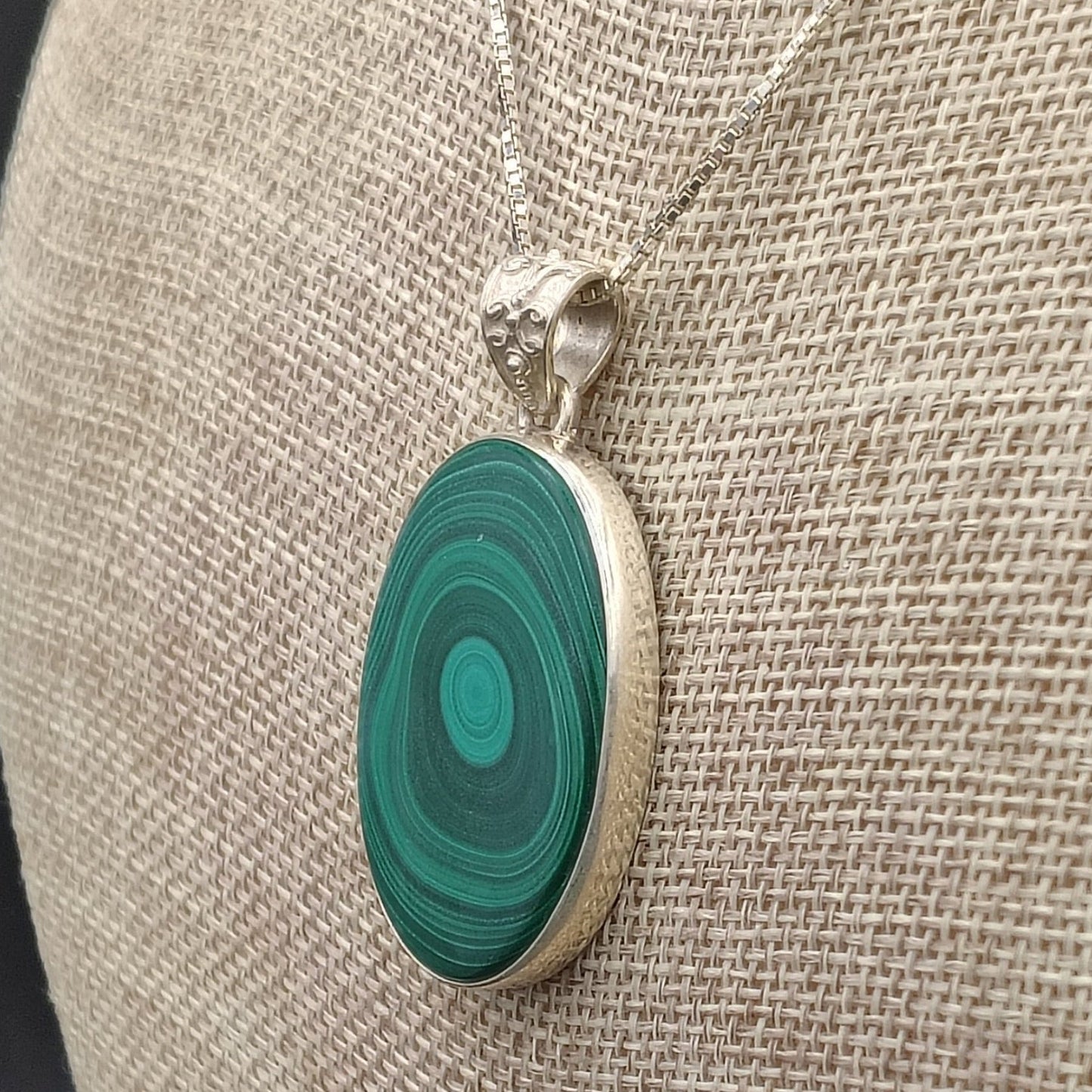 Side close up of the green Malachite pendant necklace on a beige fabric background .