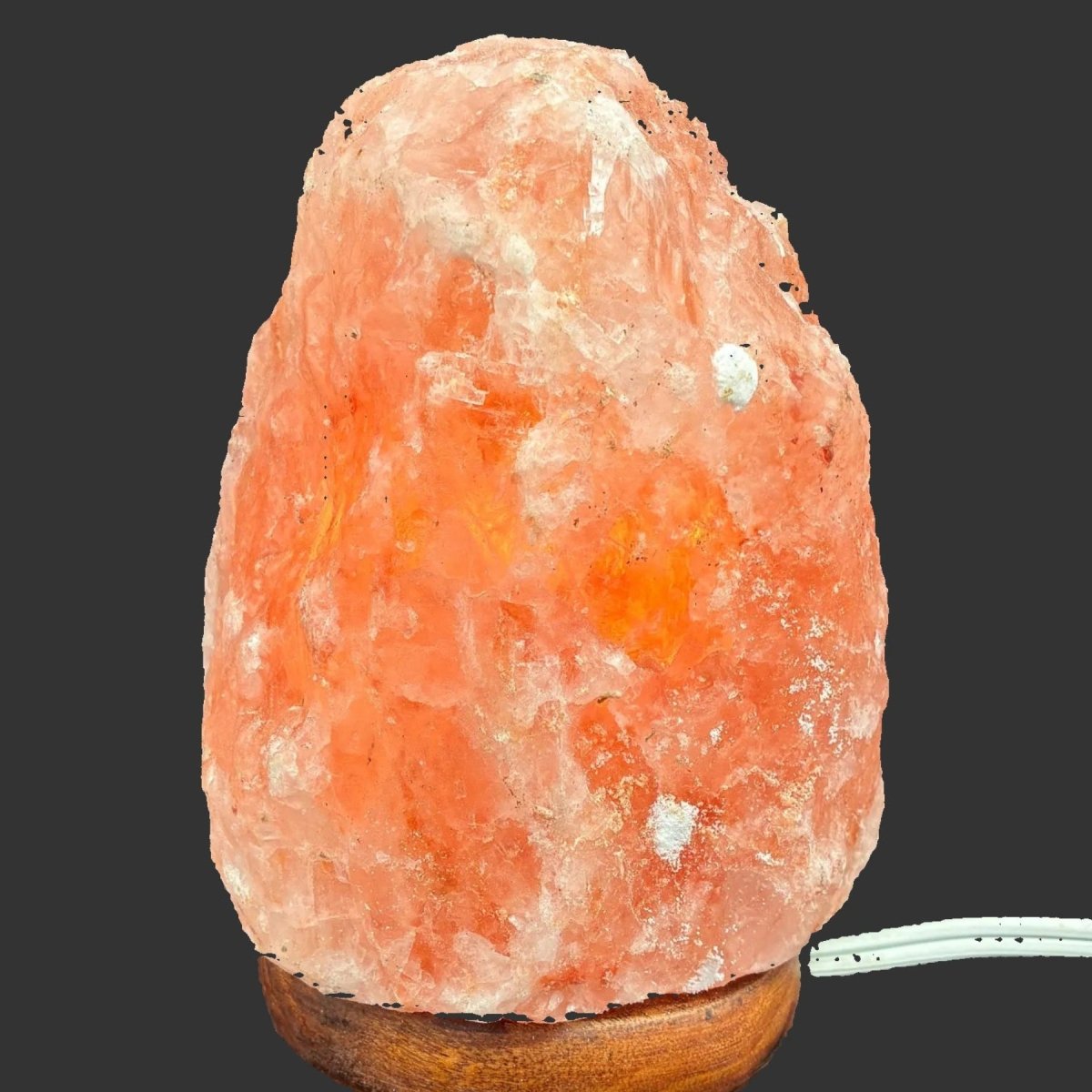 Natural pink Himalayan salt lamp with the light switch turned on, with a black and dark background.