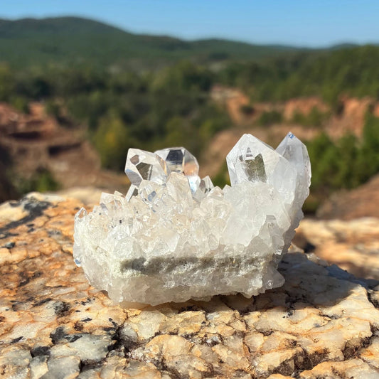 Front side of this small quartz crystal cluster on a boulder outdoors.
