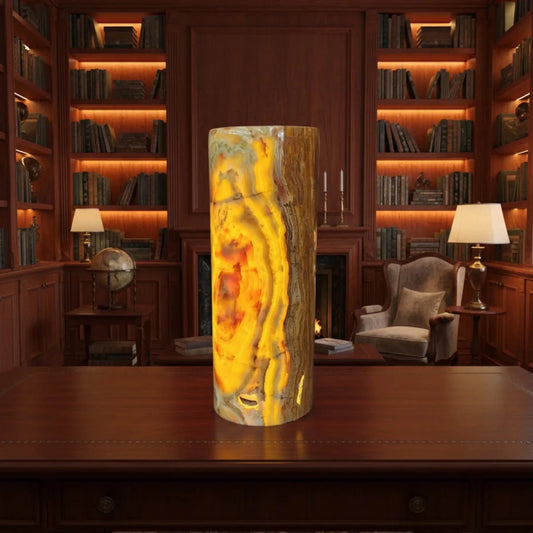 This is the polished onyx cylinder lamp with the lamp turned on, in a library.