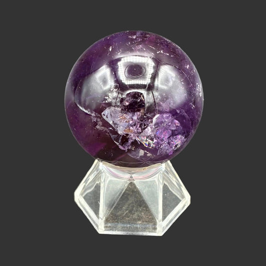 Front side of this polished Amethyst sphere on a clear acrylic stand, in front of a black background.