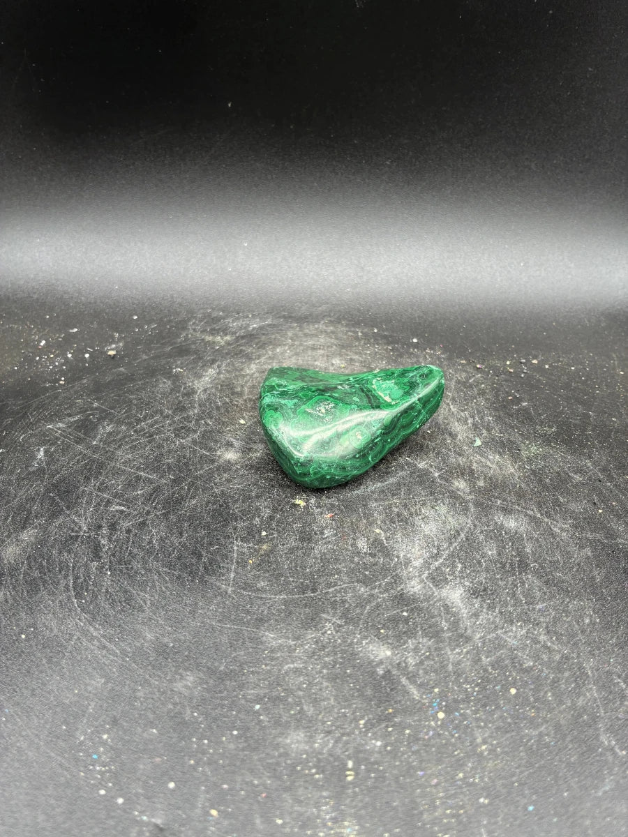 Back side of this polished green Malachite specimen, in front of a black background.