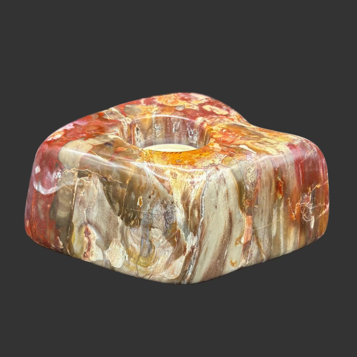 Front side of this polished petrified wood candle holder, in front of a black background.
