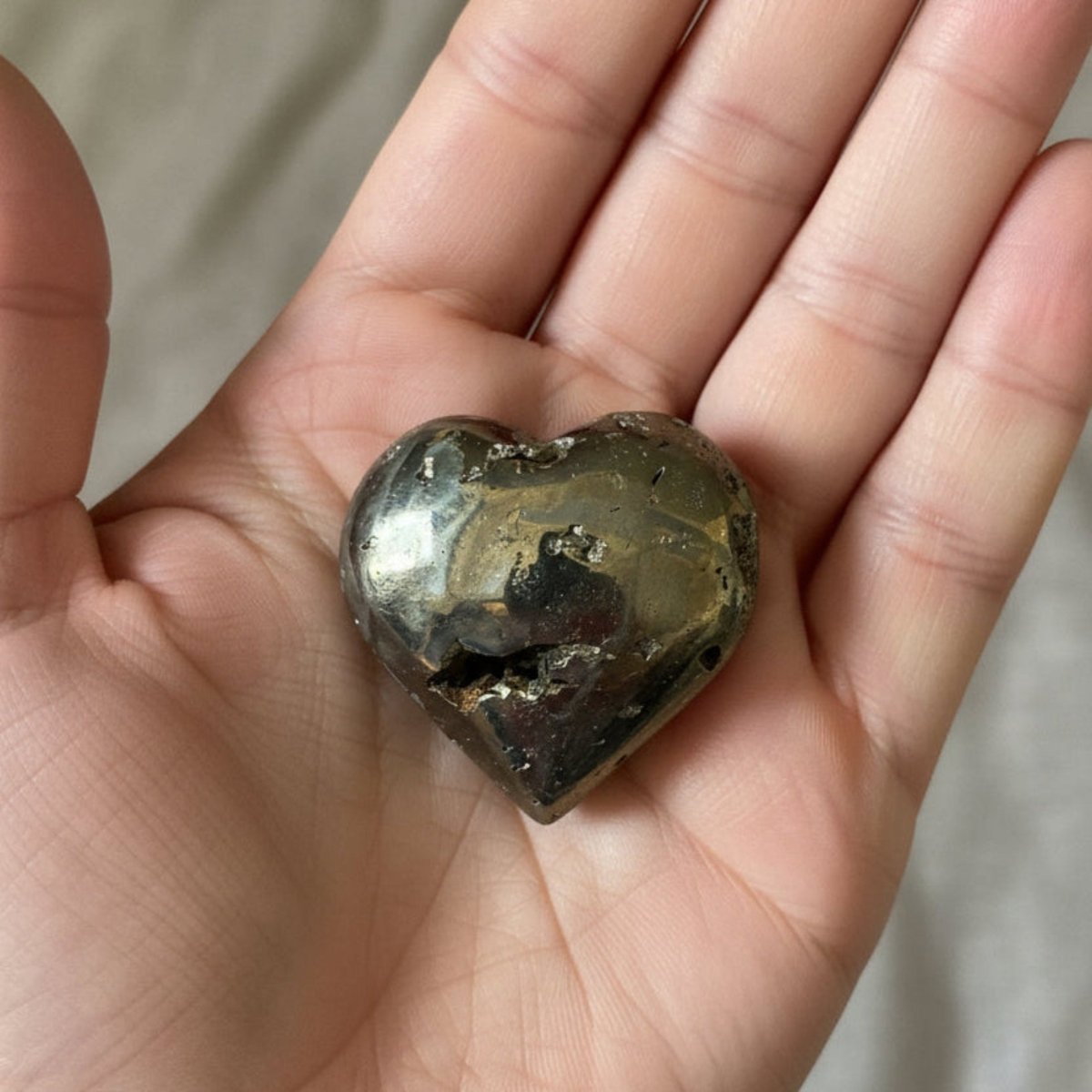 Polished gold Pyrite heart in the palm of a hand.