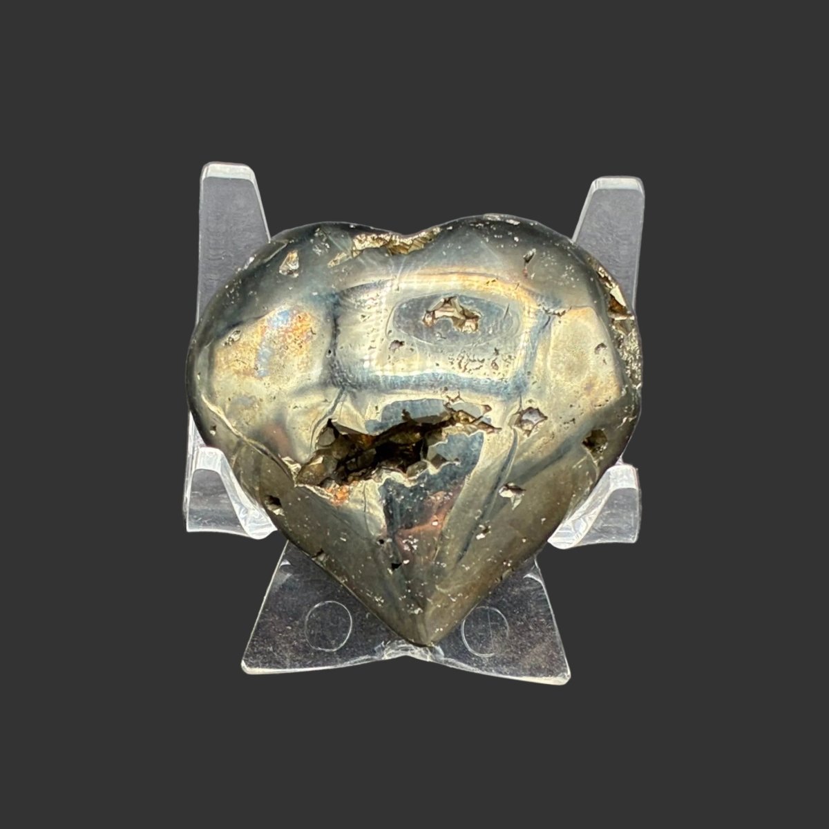Back side of this polished gold Pyrite heart, in front of a black background and on a acrylic stand.
