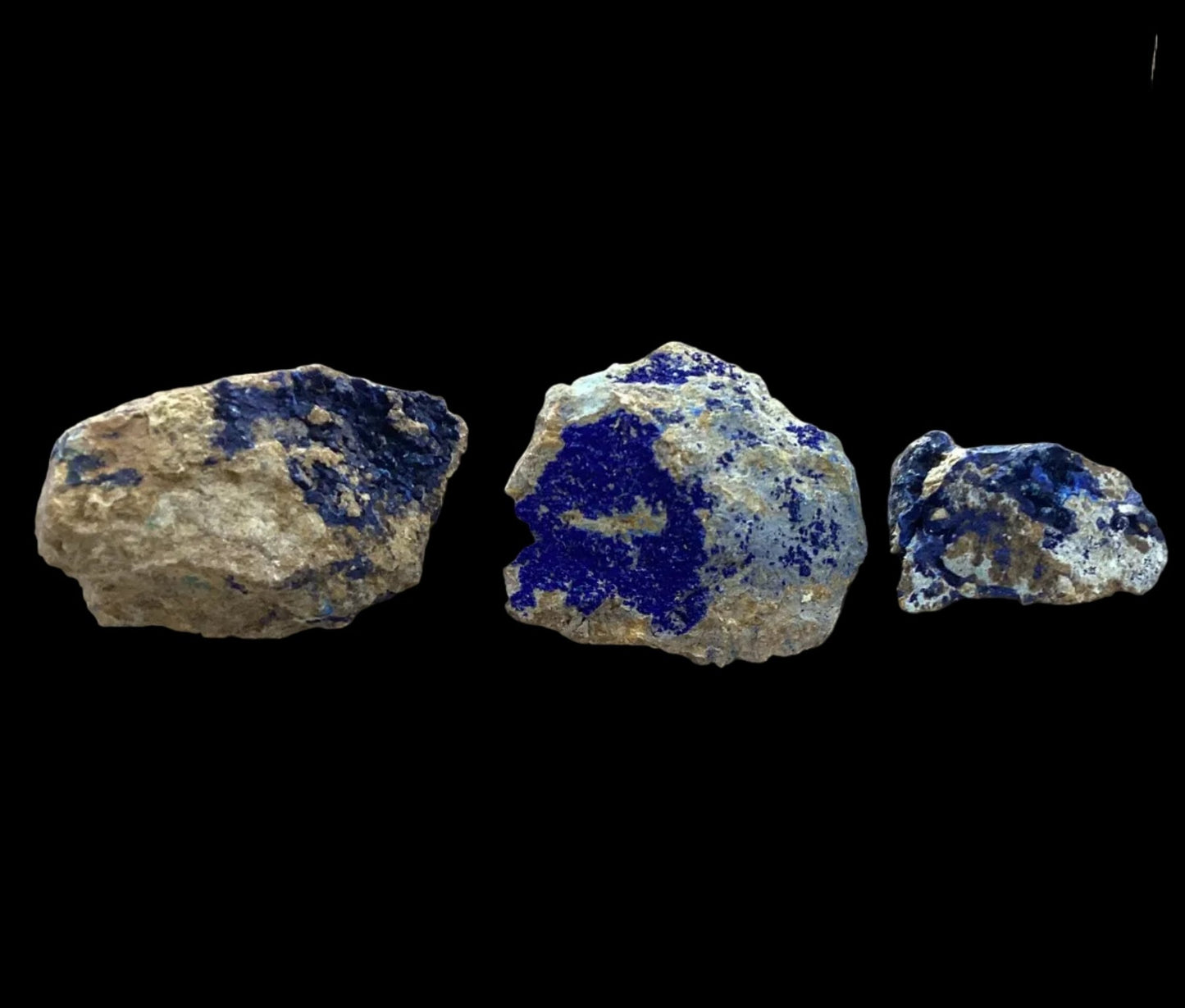 Three pieces of rock with blue mineral inclusions on a black background
