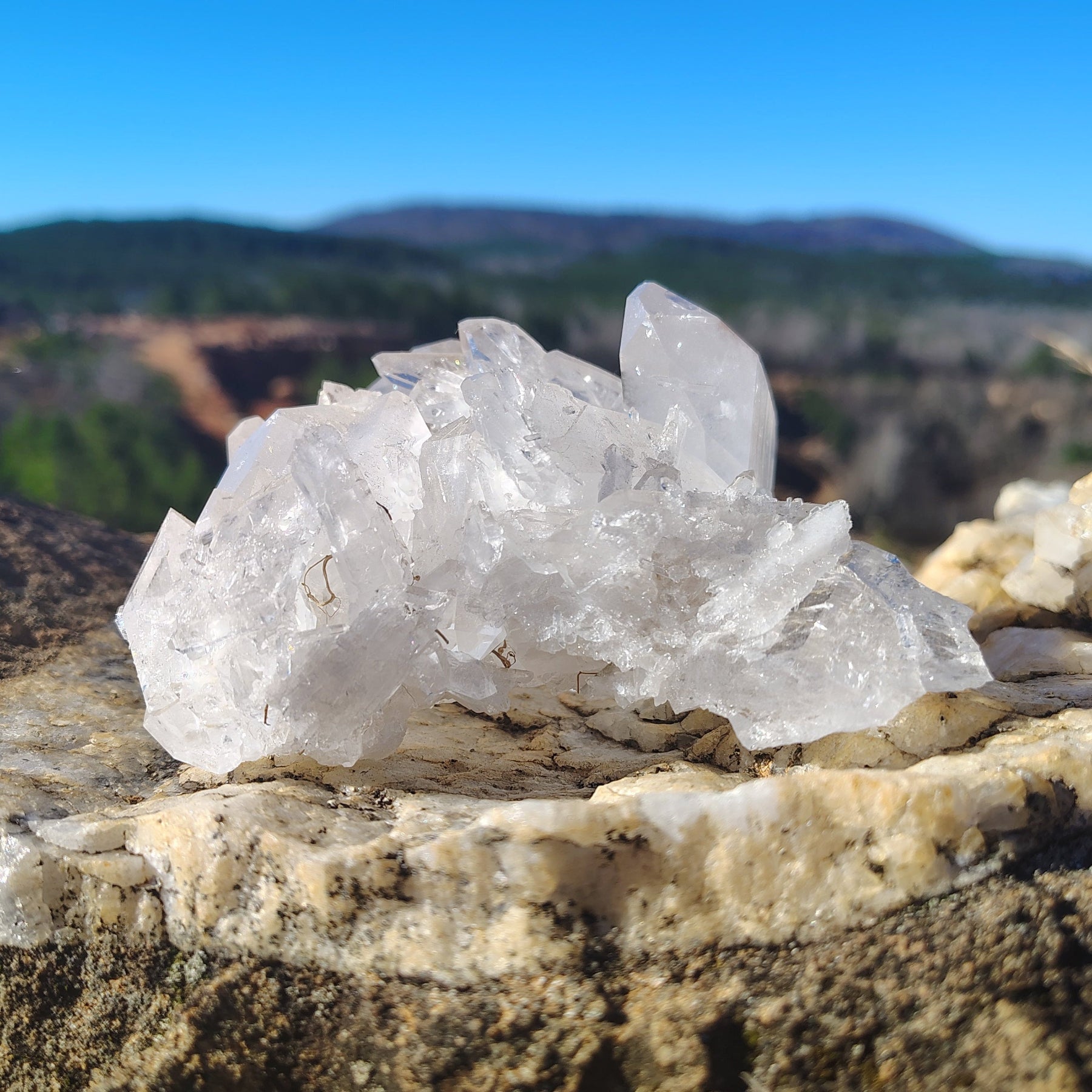 Front view of a Quartz crystal cluster on a boulder outdoors, in front of a clear blue sky.