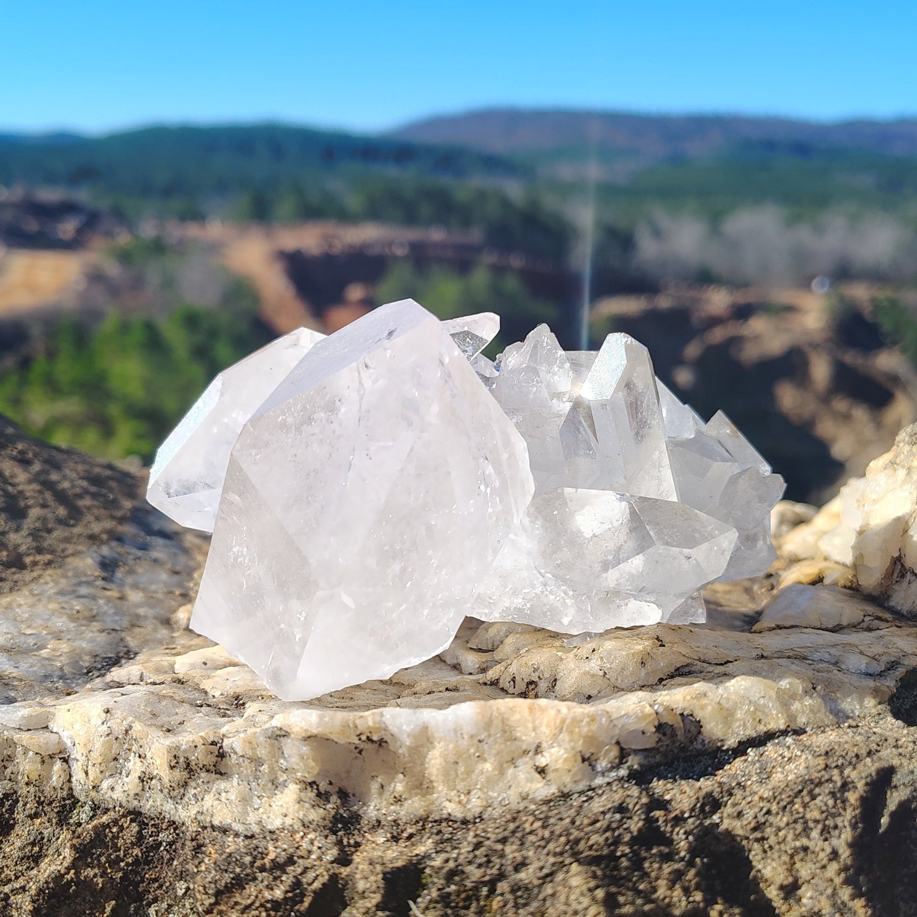 This is the back side of the Quartz crystal cluster, in front of a green landscape and a clear blue sky.