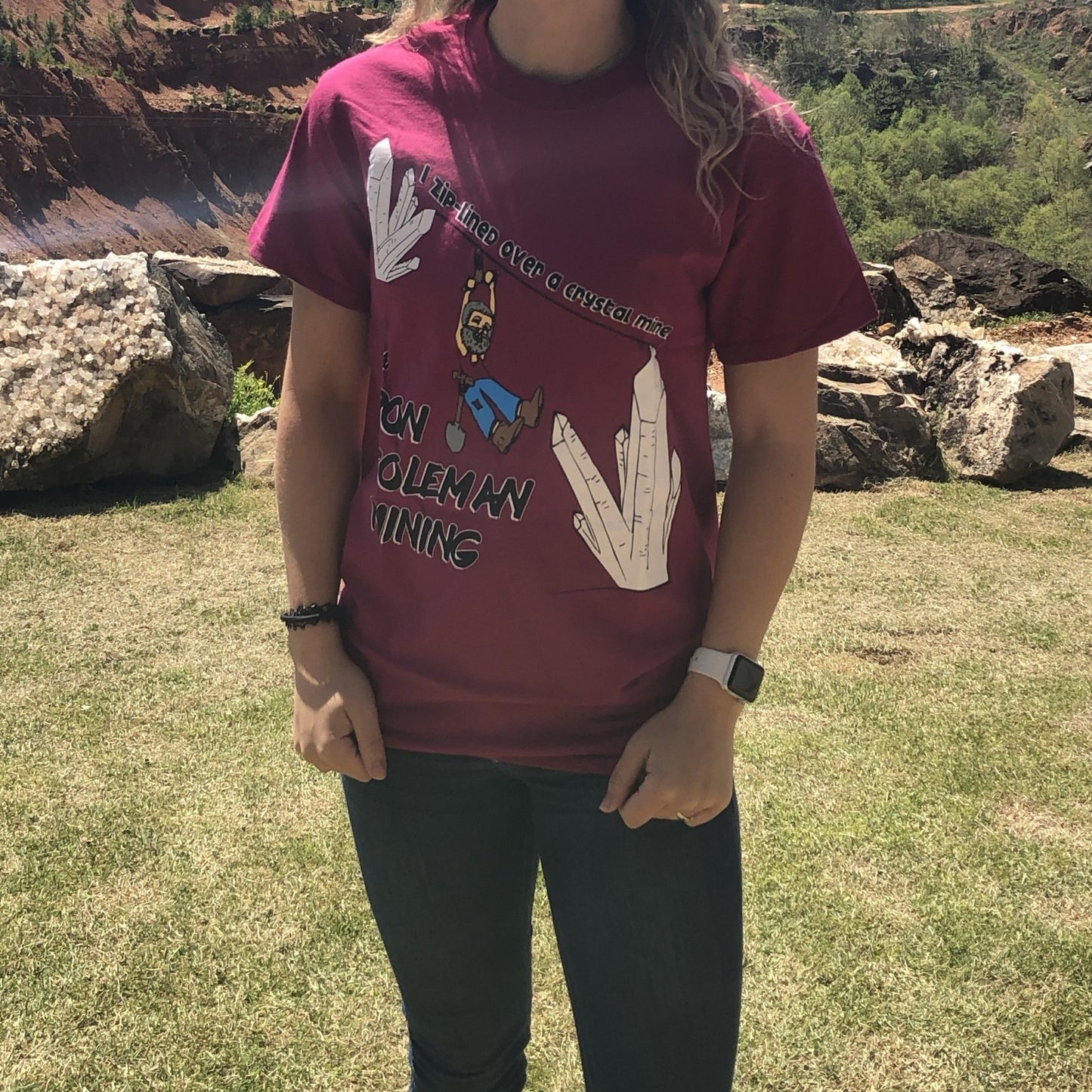 Berry color short sleeve t-shirt with Ron Coleman Miner Caricature zip-lining between two white Quartz crystal clusters