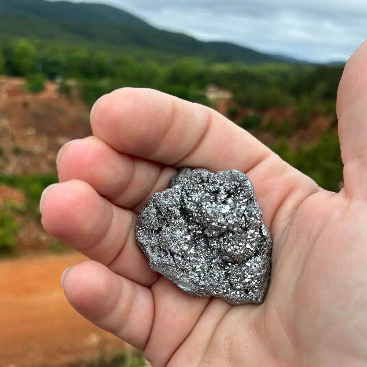 Silver aura quartz geode in a palm of a hand, in natural outdoor lighting.