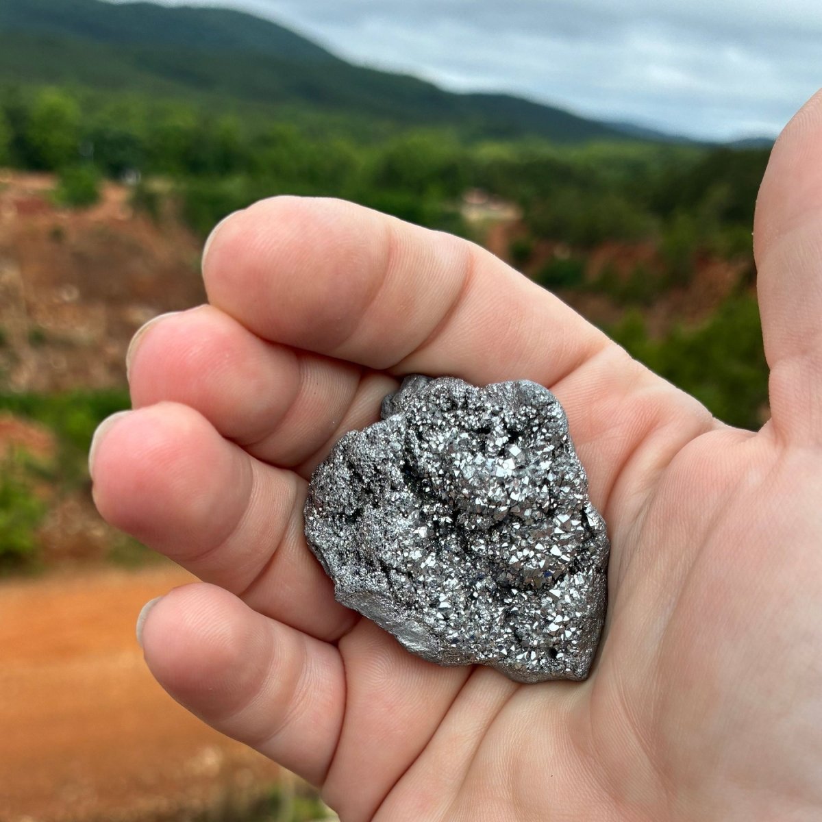 Silver aura quartz geode in a palm of a hand, in natural outdoor lighting.