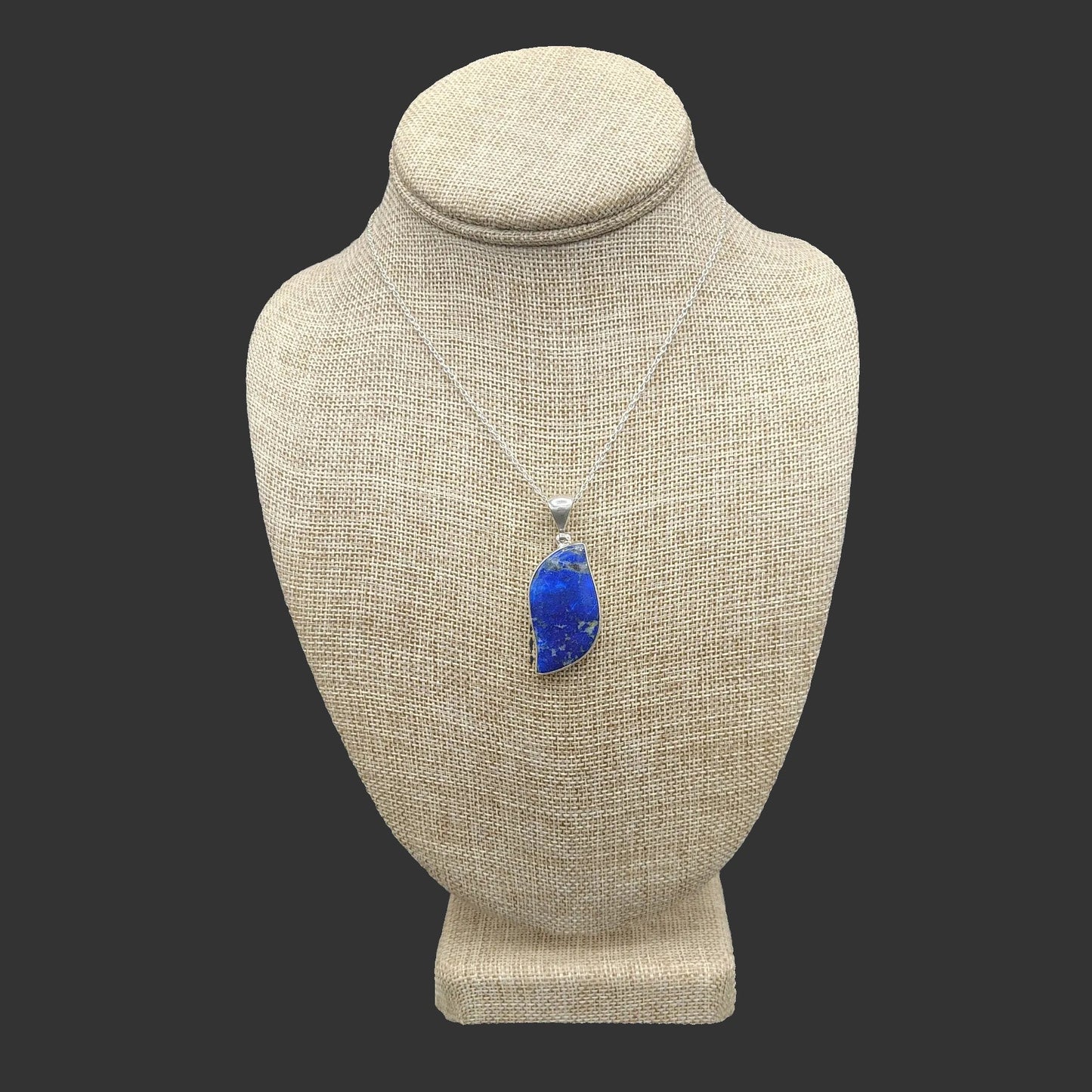 Blue lapis pendant necklace on a beige mannequin bust against a dark background.