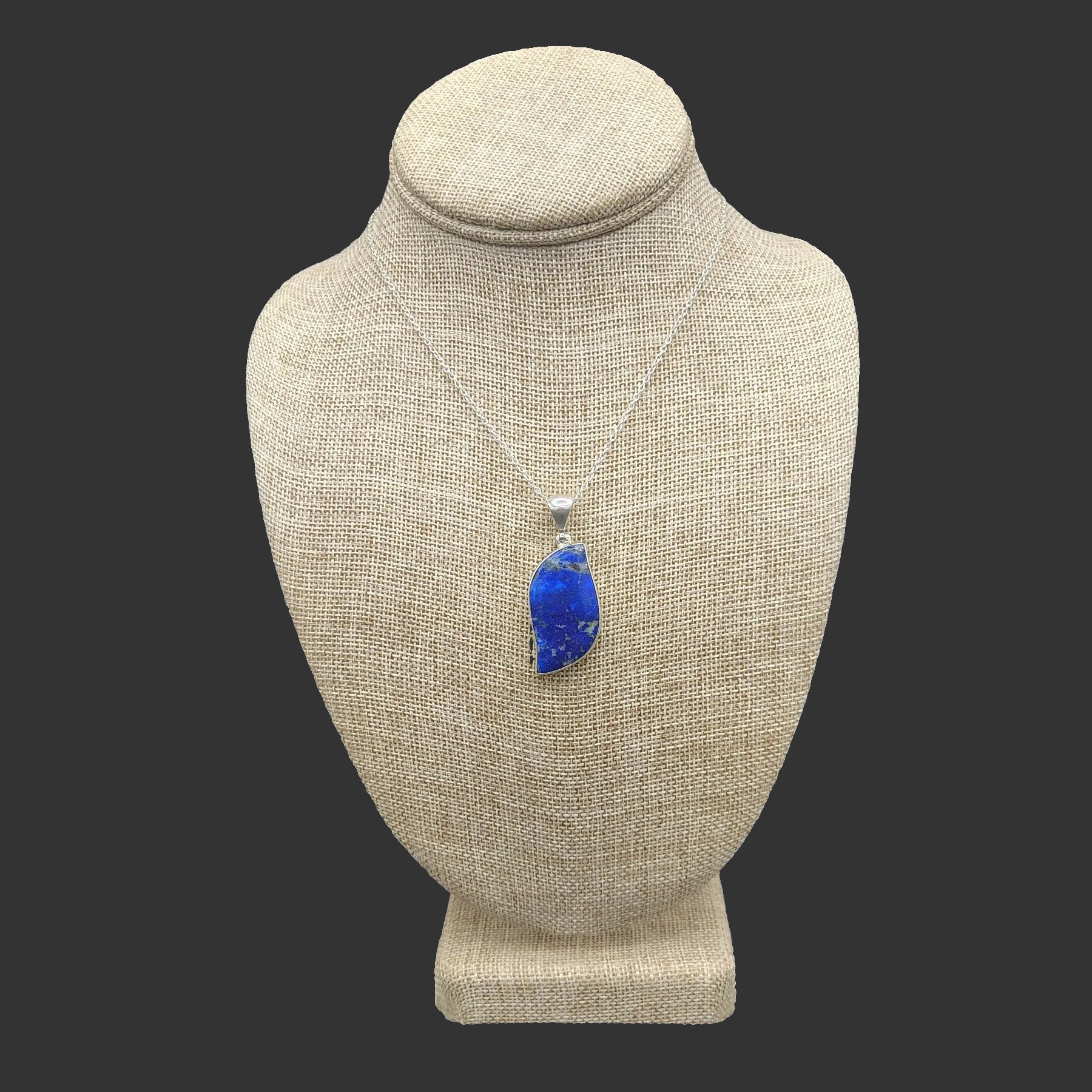 Blue lapis pendant necklace on a beige mannequin bust against a dark background.