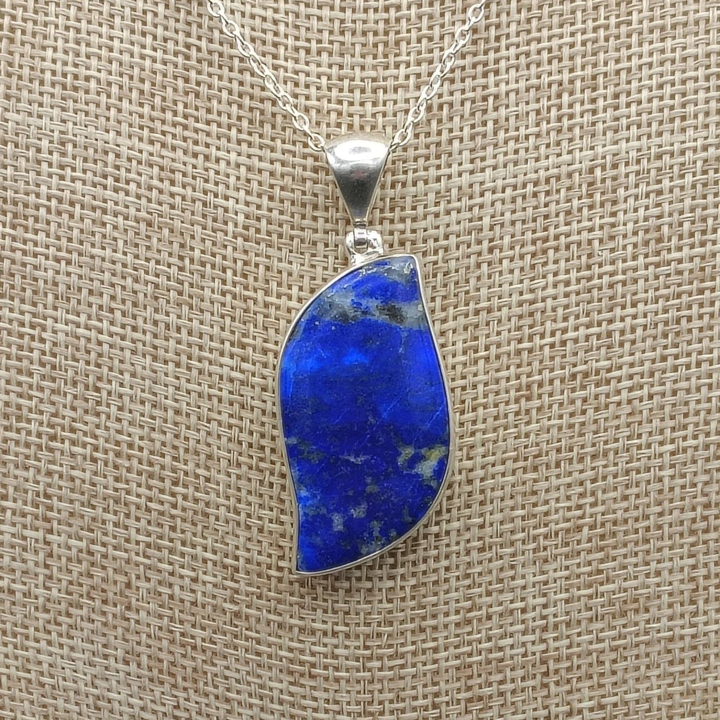 Close up of blue lapis pendant on a necklace against a beige background.