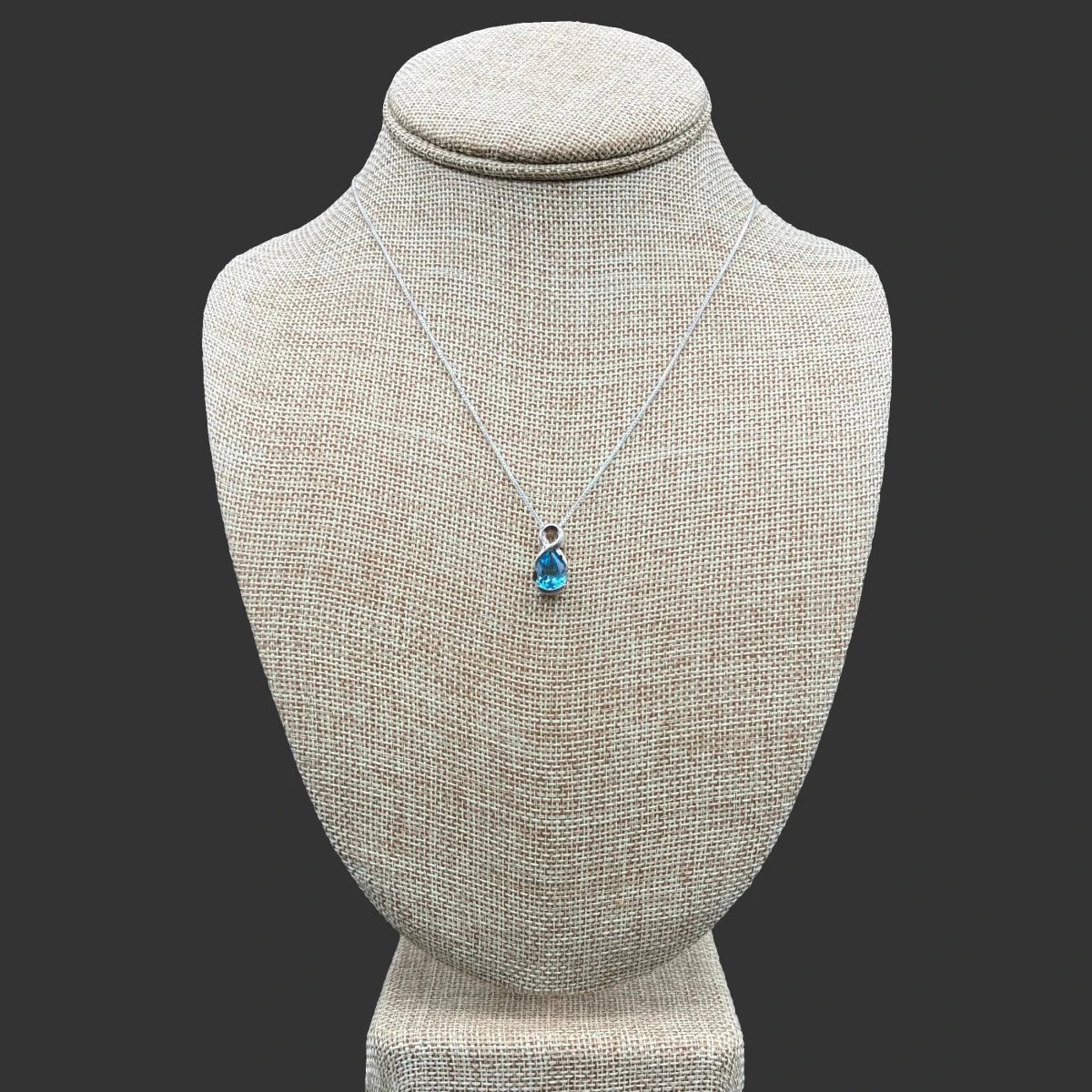 Front view of this sterling silver and blue topaz necklace, in front of a black bacground.