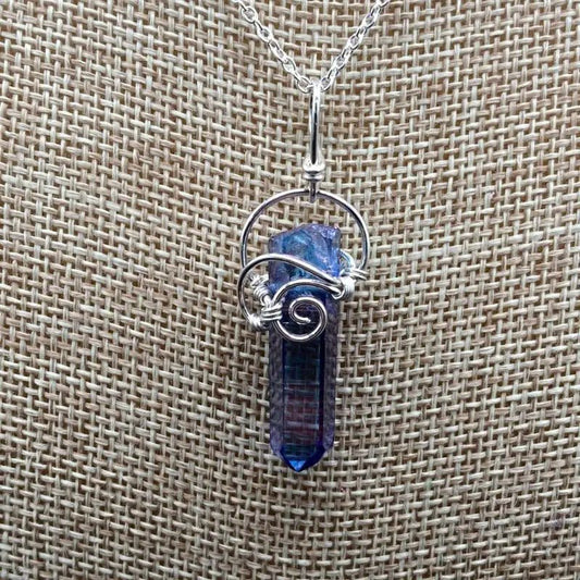 Close Up Of Aqua Aura Wire Wrapped Crystal Pendant. It Is A Bluish Purple In Color.