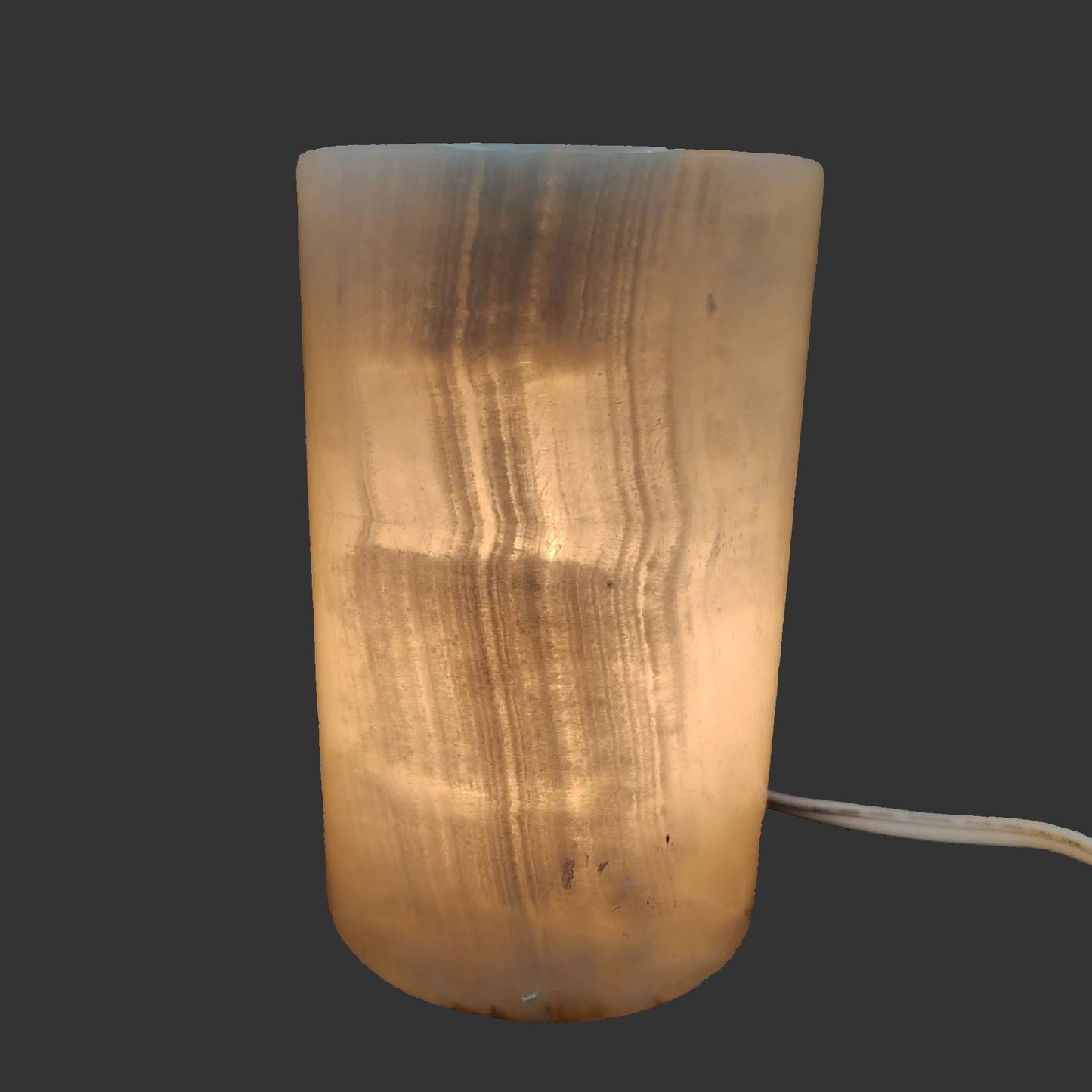 Polished cream-colored Onyx cylinder lamp, with the lamp turned on.