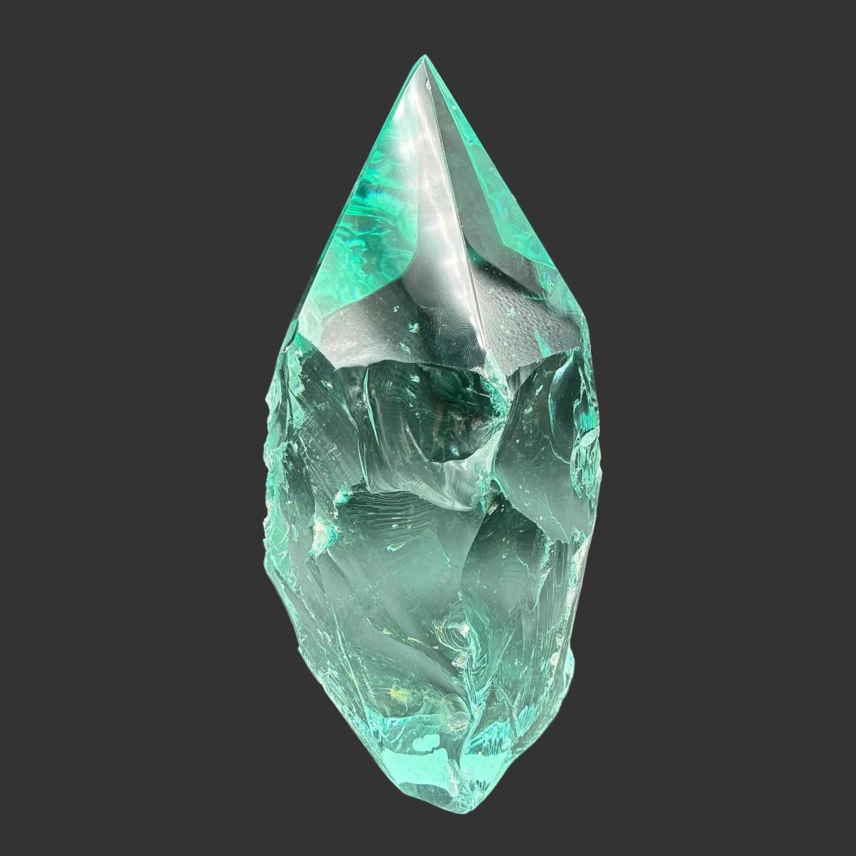 Back side of this blue green slag glass freeform, in front of a black background.