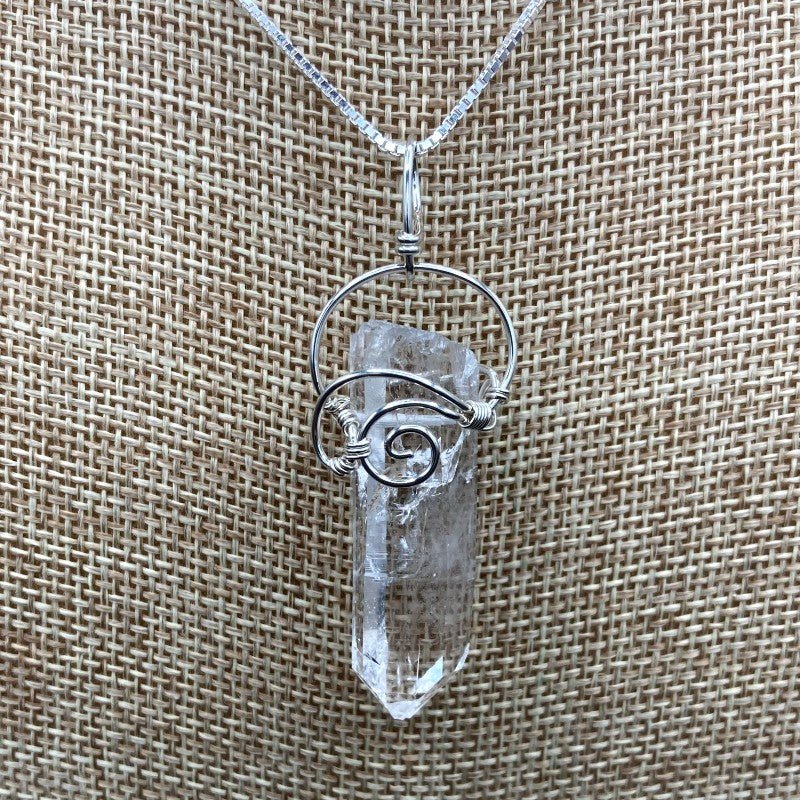 Close Up Of Crystal Point Pendant, Wrapped In Sterling Silver Wire In A Curly Design To Hold The Clear Crystal Point